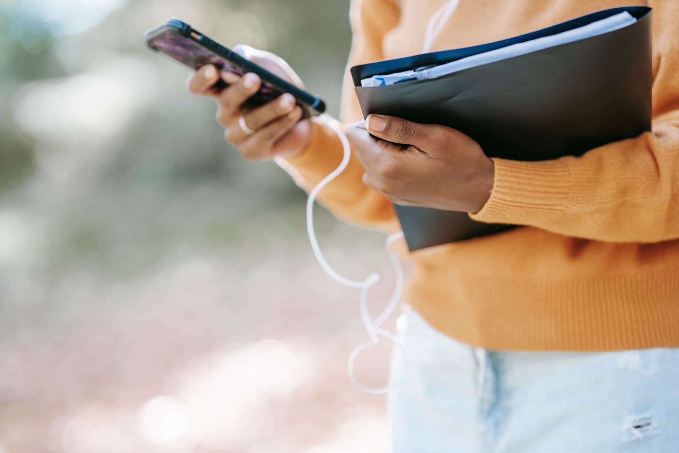 person outdoors holding a folder while checking a smartphone